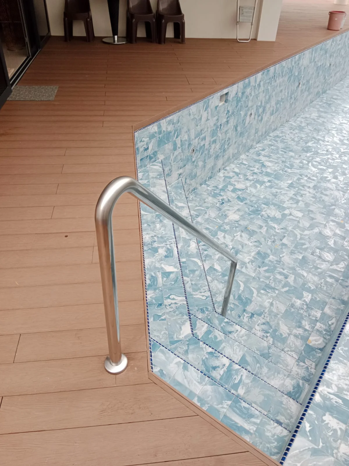 Stainless steel swimming pool stair railing installed beside a residential pool